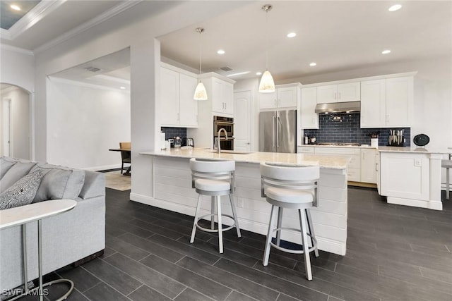 kitchen with kitchen peninsula, appliances with stainless steel finishes, decorative light fixtures, white cabinetry, and a kitchen bar