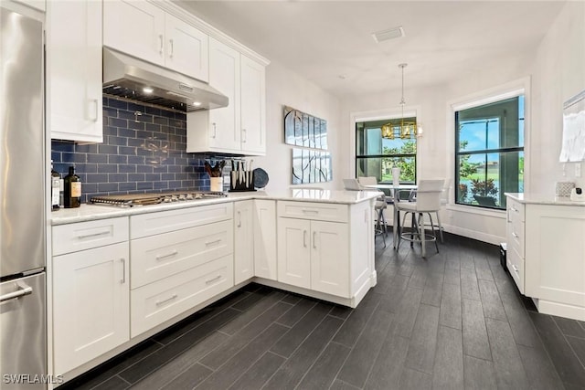 kitchen featuring kitchen peninsula, pendant lighting, appliances with stainless steel finishes, backsplash, and white cabinetry