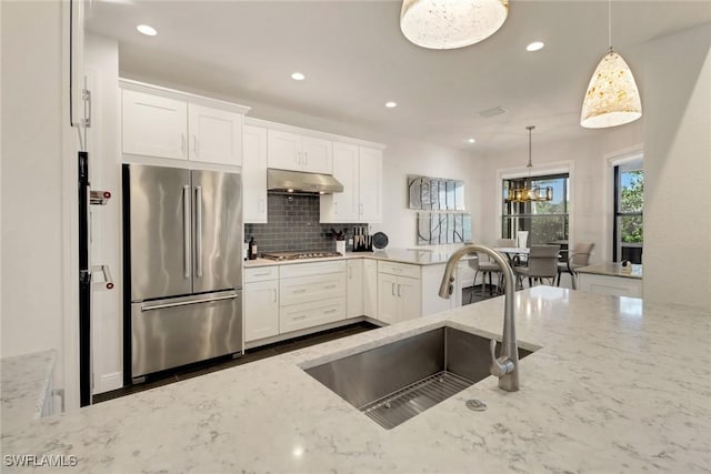 kitchen with decorative light fixtures, sink, light stone counters, and stainless steel appliances