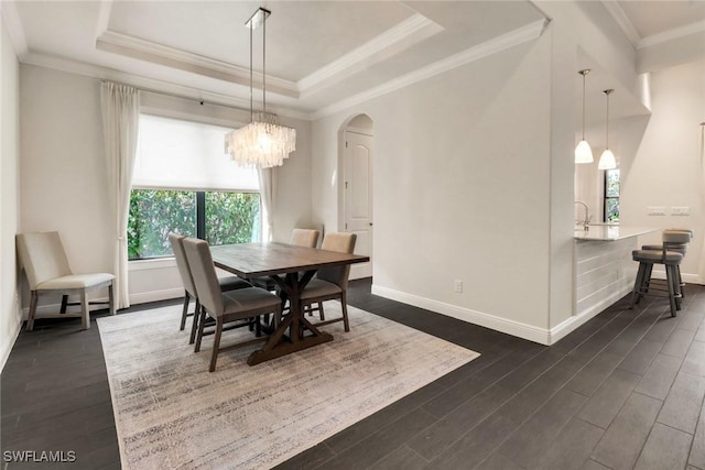 dining area with dark wood-type flooring, a tray ceiling, ornamental molding, and an inviting chandelier