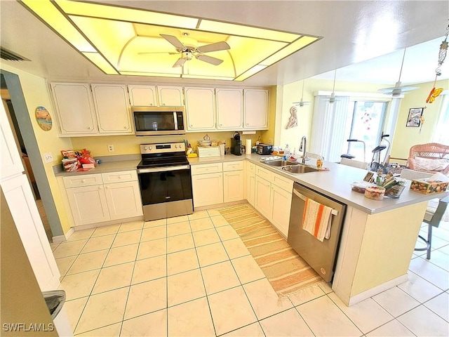 kitchen with a peninsula, a sink, a ceiling fan, appliances with stainless steel finishes, and a raised ceiling