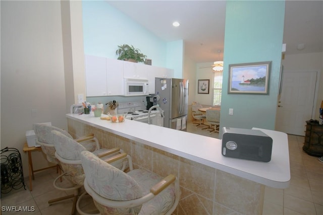 kitchen with a breakfast bar area, kitchen peninsula, white cabinets, and white appliances