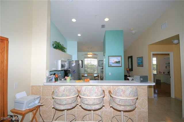 kitchen featuring ceiling fan, kitchen peninsula, stainless steel fridge, vaulted ceiling, and light tile patterned floors