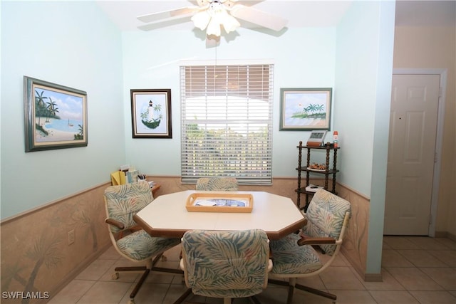 tiled dining space with ceiling fan and wood walls