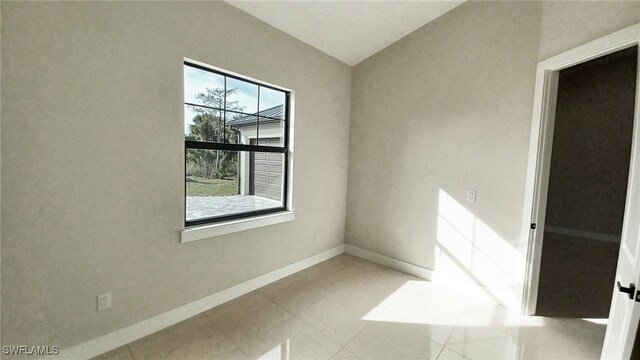 tiled spare room featuring lofted ceiling