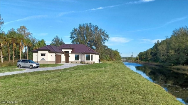 view of front of house with stucco siding, a water view, a front lawn, a standing seam roof, and metal roof