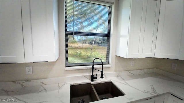 kitchen with white cabinetry, sink, light stone counters, and a healthy amount of sunlight