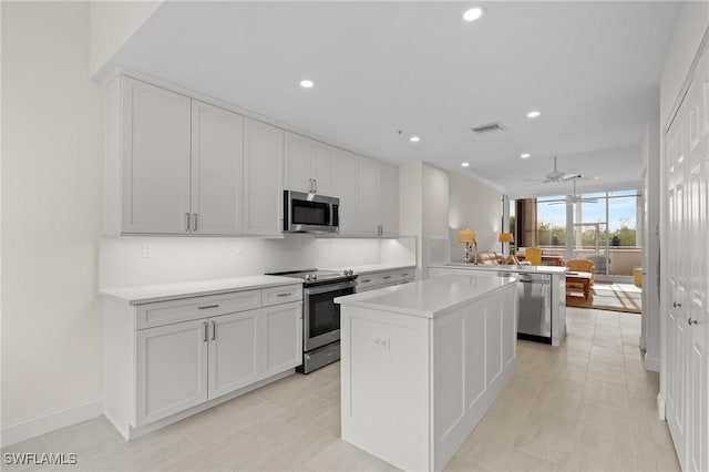 kitchen featuring white cabinets, ceiling fan, appliances with stainless steel finishes, a kitchen island, and kitchen peninsula