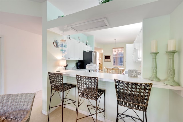 kitchen with white cabinets, stainless steel fridge, kitchen peninsula, and a breakfast bar area