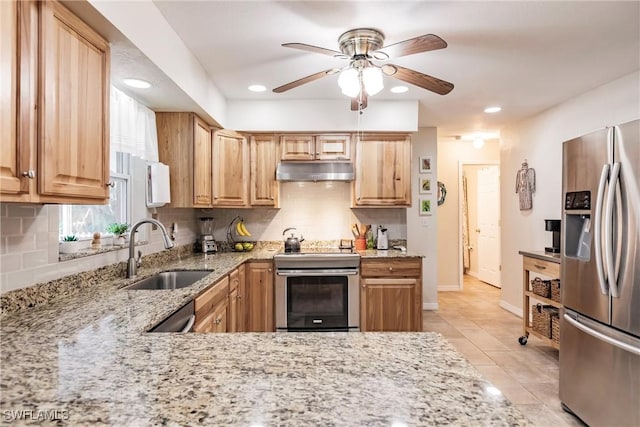 kitchen featuring ceiling fan, sink, stainless steel appliances, tasteful backsplash, and light stone counters