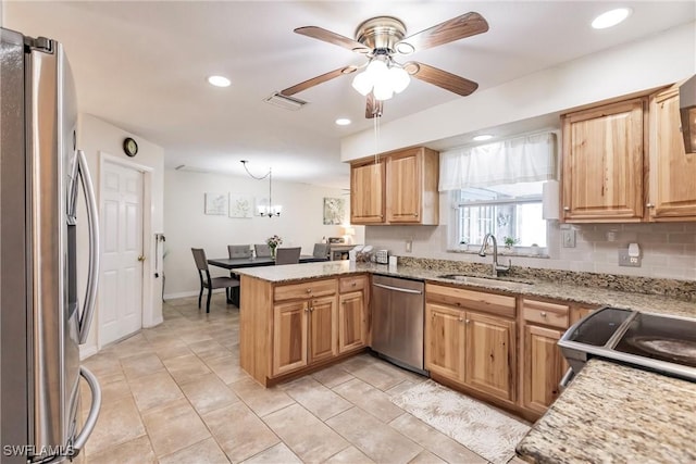 kitchen with kitchen peninsula, ceiling fan with notable chandelier, stainless steel appliances, sink, and hanging light fixtures