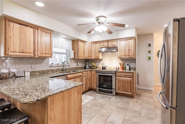 kitchen featuring kitchen peninsula, light stone counters, stainless steel appliances, ceiling fan, and sink