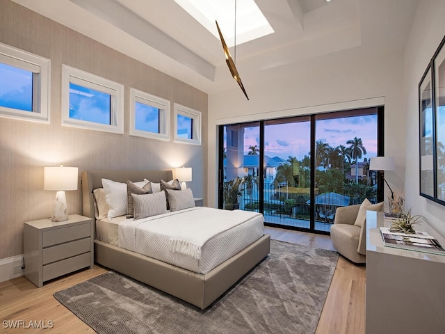 bedroom featuring access to outside, light hardwood / wood-style floors, and a raised ceiling