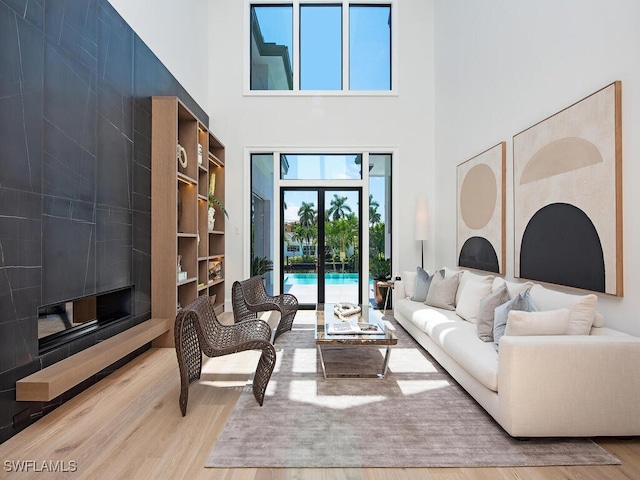 living room with built in shelves, a tiled fireplace, a towering ceiling, and light hardwood / wood-style flooring