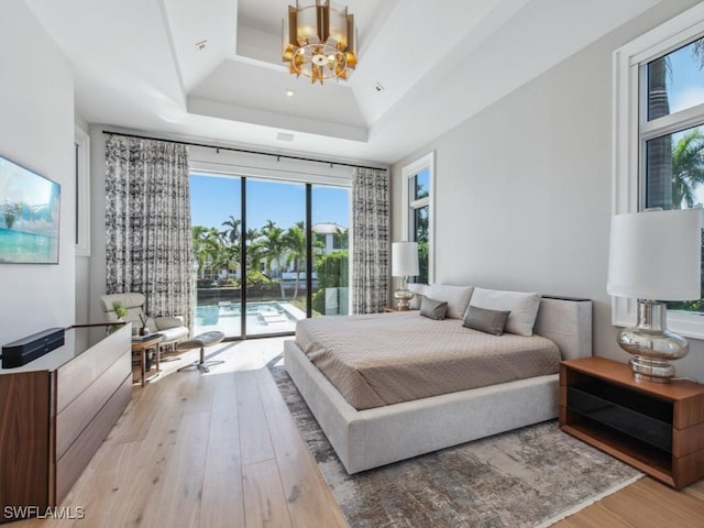 bedroom featuring access to exterior, light hardwood / wood-style floors, a raised ceiling, and a chandelier