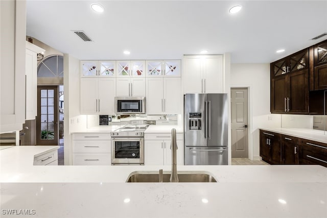 kitchen featuring white cabinets, appliances with stainless steel finishes, dark brown cabinetry, and sink