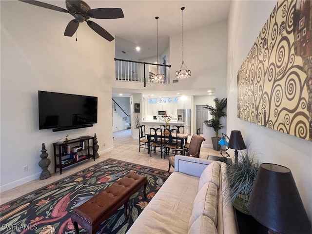 living room with light tile patterned floors, ceiling fan with notable chandelier, and a high ceiling