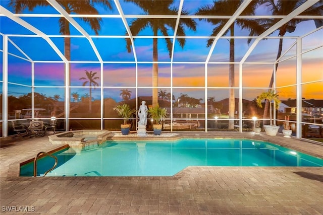 pool at dusk featuring an in ground hot tub, glass enclosure, and a patio