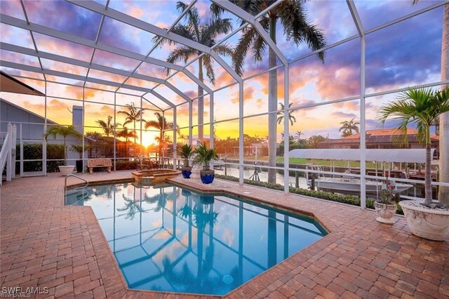 pool at dusk featuring a hot tub, a lanai, and a patio area