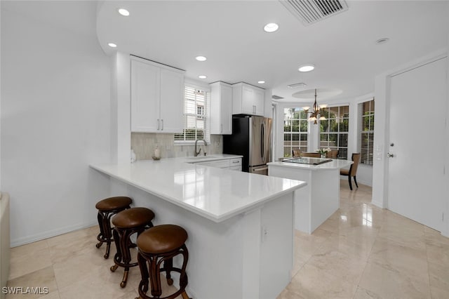 kitchen with white cabinetry, tasteful backsplash, kitchen peninsula, stainless steel fridge, and decorative light fixtures