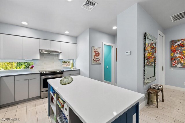 kitchen with white cabinetry, tasteful backsplash, light hardwood / wood-style floors, stainless steel electric stove, and a kitchen island