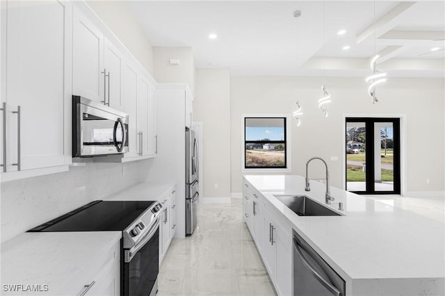 kitchen featuring light stone countertops, stainless steel appliances, sink, white cabinetry, and hanging light fixtures