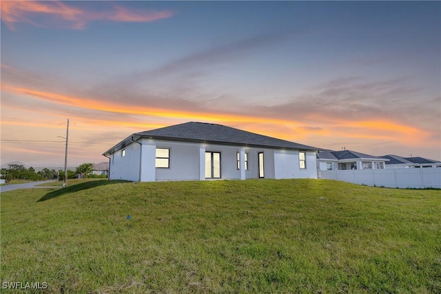 back house at dusk featuring a lawn