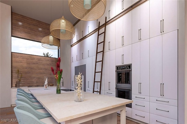 kitchen with a towering ceiling, white cabinets, double oven, and decorative light fixtures