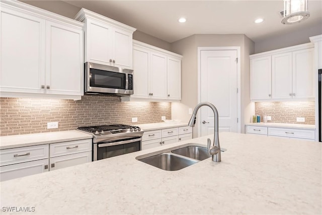 kitchen with tasteful backsplash, stainless steel appliances, sink, white cabinetry, and hanging light fixtures