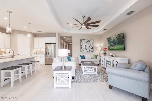 living room with ceiling fan, a raised ceiling, and sink