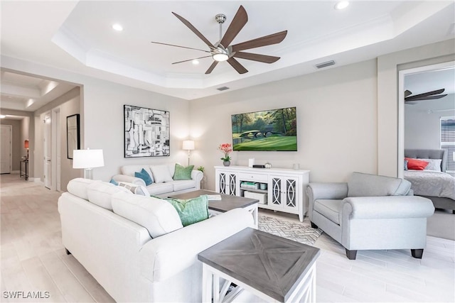 living room with ceiling fan, light hardwood / wood-style floors, and a tray ceiling