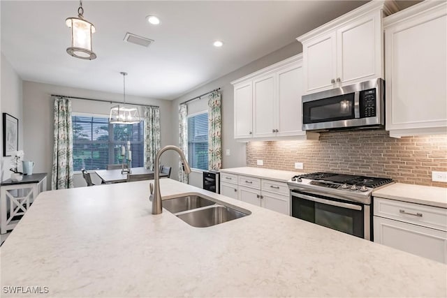 kitchen featuring white cabinetry, sink, backsplash, decorative light fixtures, and appliances with stainless steel finishes