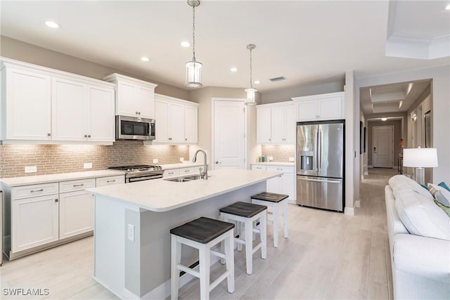 kitchen with appliances with stainless steel finishes, white cabinetry, a kitchen island with sink, and pendant lighting