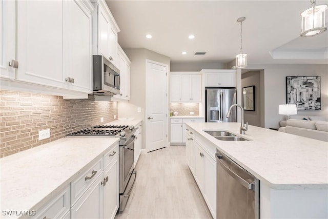 kitchen featuring a center island with sink, hanging light fixtures, sink, appliances with stainless steel finishes, and white cabinetry