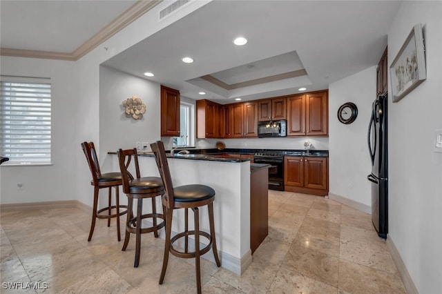 kitchen with a raised ceiling, kitchen peninsula, a kitchen bar, black appliances, and ornamental molding