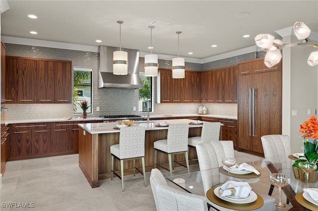 kitchen featuring a center island, wall chimney exhaust hood, pendant lighting, stainless steel gas stovetop, and a breakfast bar