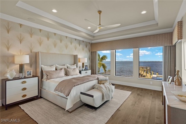 bedroom with hardwood / wood-style floors, a water view, a raised ceiling, and ceiling fan