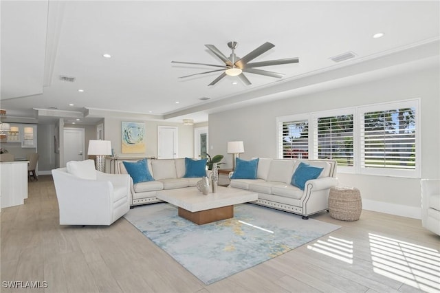 living room with a tray ceiling, ceiling fan, and light wood-type flooring