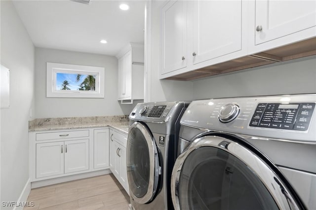 clothes washing area featuring cabinets, washing machine and clothes dryer, and light wood-type flooring