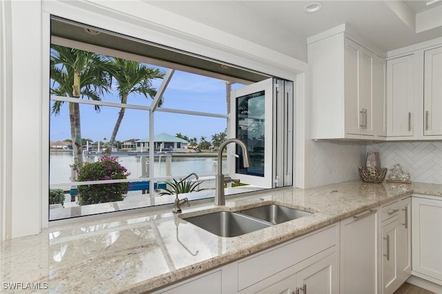 kitchen with tasteful backsplash, sink, white cabinets, a water view, and light stone countertops