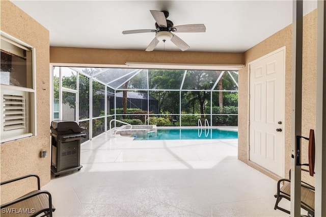 view of pool with grilling area, glass enclosure, ceiling fan, and a patio area