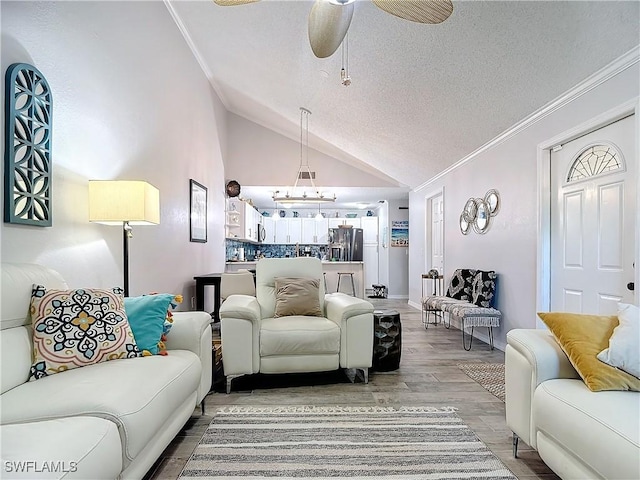 living room with ceiling fan, hardwood / wood-style floors, a textured ceiling, vaulted ceiling, and ornamental molding