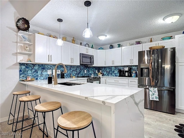 kitchen featuring kitchen peninsula, a textured ceiling, stainless steel appliances, and white cabinetry