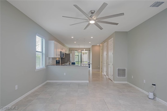 interior space with stainless steel appliances, tasteful backsplash, kitchen peninsula, white cabinets, and ceiling fan with notable chandelier