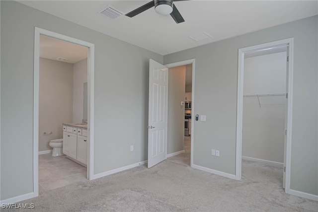 unfurnished bedroom with ensuite bathroom, ceiling fan, a spacious closet, light colored carpet, and a closet