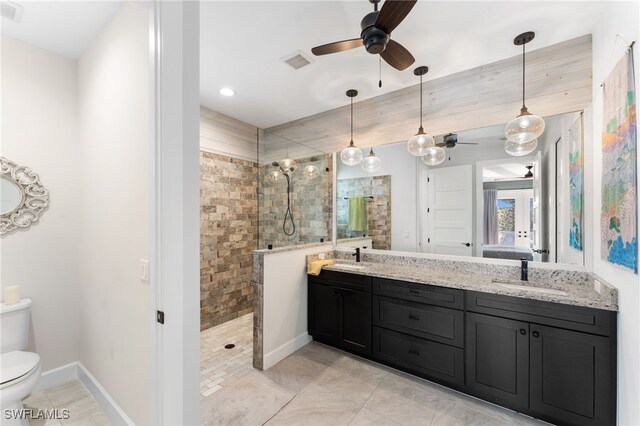 bathroom featuring a tile shower, ceiling fan, vanity, and toilet