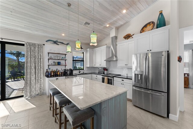 kitchen with stainless steel appliances, wall chimney range hood, pendant lighting, white cabinets, and a kitchen island