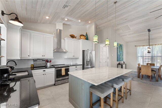 kitchen featuring white cabinets, pendant lighting, stainless steel appliances, and wall chimney range hood