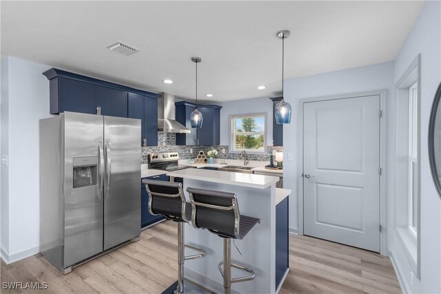 kitchen featuring sink, stainless steel appliances, wall chimney range hood, blue cabinets, and pendant lighting