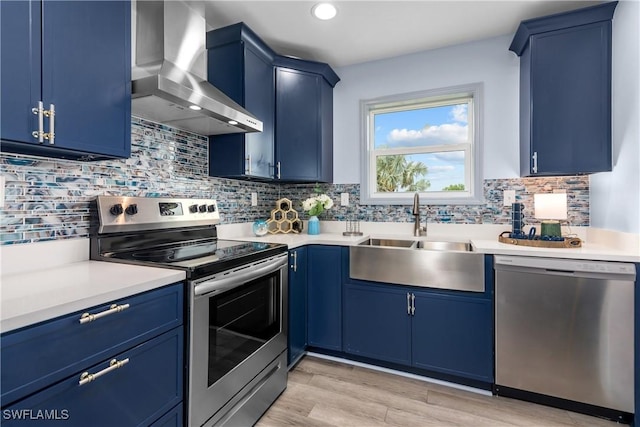 kitchen with blue cabinetry, sink, wall chimney range hood, and stainless steel appliances